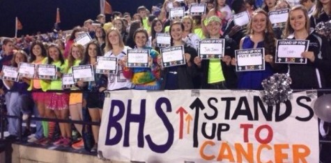 Students at the football game holding signs to stand up to cancer
