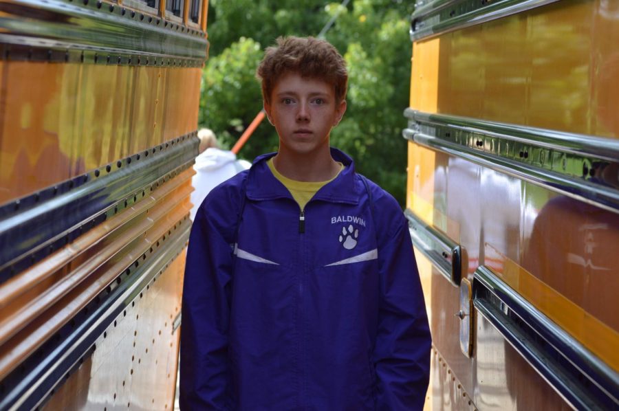 Jairub Constable stands between two school buses at the Sabetha Cross Country Meet, 2019.