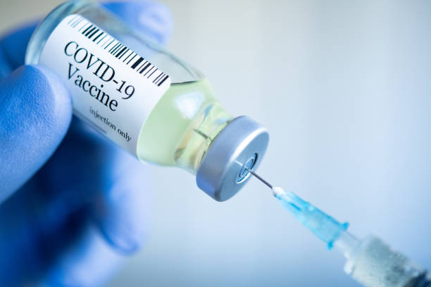 Doctor drawing up Covid-19 vaccine from glass phial bottle and filling syringe injection for vaccination. Close up of hand wearing protective disposable gloves in lab and holding a bottle of vaccination drugs. Hand with blue surgical gloves taking sars-coV-2 vaccine dose from vial with syringe: prevention and immunization concept.